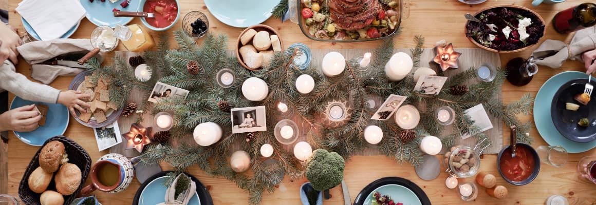 Table set for Christmas dinner with a large centerpiece of candles and evergreen boughs